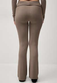 Brune flagede bukser lavet af et blødt, strækbart materiale, med en bred talje og en glat, ensartet overflade.