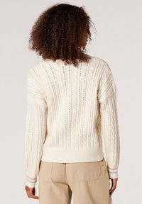 Cremefarbener Strickpullover mit Kabelmuster, geripptem Saum und Bündchen, der ein strukturiertes Muster und subtile Pastellstreifen an den Kanten der Bündchen aufweist.