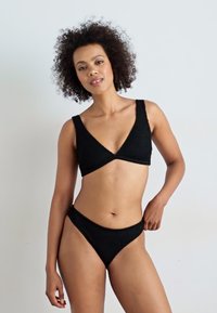 Czarny komplet bikini z teksturowanej tkaniny. Górna część ma dekolt w kształcie v z szerokimi ramiączkami, a dolna część jest nisko osadzona z minimalnym zakryciem.