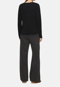 Schwarzes Langarmshirt mit rundem Ausschnitt, kombiniert mit dunklen, hoch taillierten, weit geschnittenen Hosen und hellbraunen Schuhen. Glatter Stoff.