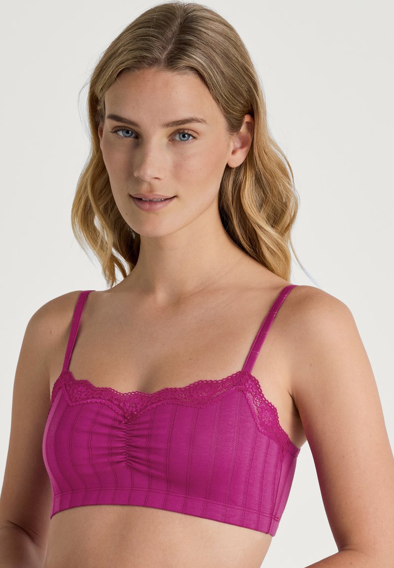 Fuchsia lace-trimmed bralette with ruched center and thin adjustable straps; made from a smooth stretch fabric with subtle vertical lines.