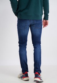 Blå slim jeans med en urtvättad look och bakfickor. Matchas med grå och röda sneakers. Modellen står, vänd bort.