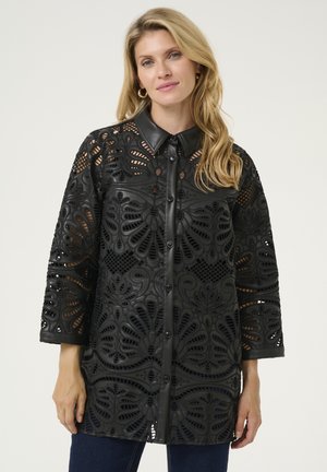 Tunic nera tagliata al laser con colletto, caratterizzata da intricati motivi floreali, maniche a trequarti e chiusura con bottoni. Materiale in pelle testurizzata.