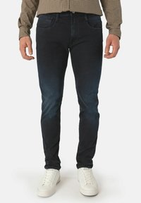 Mørke denim skinny jeans med en glatt tekstur, med fem lommer og subtile falming detaljer, sammen med hvite joggesko.