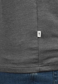 Temno siva bombažna majica z gladko teksturo, z belim etiketom s klicajem, všitim na robu.