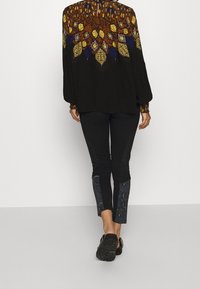Blusa nera con motivo geometrico colorato nella parte superiore, abbinata a pantaloni neri con pannelli testurizzati e scarpe nere.