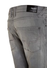 Šedé džíny z denimu s texturovaným povrchem, dekoračním šitím a černou koženou etiketou na pase. Obsahují standardní zadní kapsy.