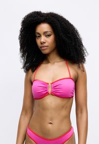 Rosa bikini topp med ribbet tekstur, med en nøkkelhulldetalj i midten og røde aksenter. Stroppene er tynne, noe som gir et minimalistisk design.