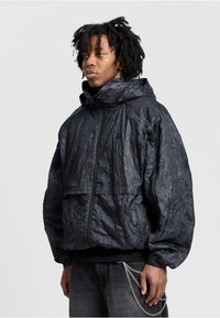 Schwarzer, zerknitterter Stoffhoodie mit hohem Kragen, Frontreißverschluss und elastischen Bündchen. Verfügt über eine frontale Tasche und einen lockeren Schnitt.