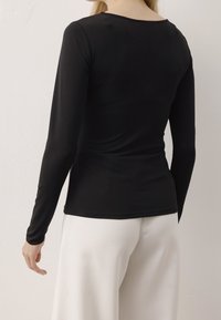 Maglietta nera a maniche lunghe realizzata in tessuto morbido, con scollatura a girocollo, forma aderente e design minimalista. Abbinata a pantaloni bianchi.