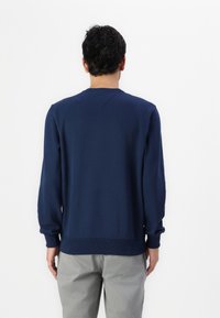 Sudadera azul marino con cuello redondo, mangas largas y puños y dobladillo acanalados. Textura suave, diseño sencillo y sin patrones visibles.