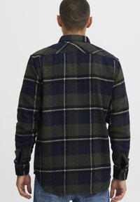 Heren geruite shirt in marineblauw en olijfgroen. Gemaakt van flanel, met een knoopmanchet, rechte snit en contrasterend geruit patroon.