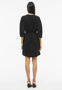 Czarna sukienka o luźnym kroju, z rękawami o długości trzy czwarte, taliowana, z plisami z tyłu. Zestawiona z czarnymi szpilkami.