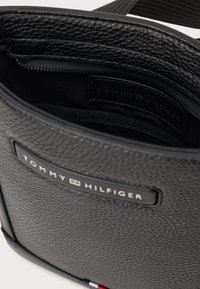 Zwarte leren tas met een gestructureerd oppervlak, voorzien van een opvallend TOMMY HILFIGER-logo en een ritsvak aan de binnenkant. Rood, wit en blauw accent.