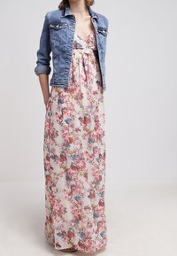 Robe maxi florale en tissu léger avec des motifs roses et bleus, design à couches, complétée par une veste en denim bleu clair.