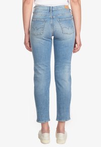Helle blaue hochgeschnittene Jeans mit schlankem Schnitt, ausgestattet mit zwei Gesäßtaschen und einem charakteristischen Nahtmuster. Der Saum ist leicht verkürzt.