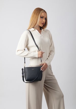 Borsa a tracolla in pelle nera con finitura testurizzata, accessori in tonalità oro e tracolla regolabile. Posizionata accanto a un modello in abbigliamento neutro.