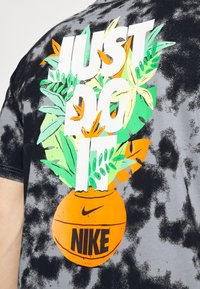 Camiseta de teñido anudado en negro y gris con gráfico floral colorido y el texto "JUST DO IT" sobre un balón de baloncesto naranja con el logotipo de Nike.