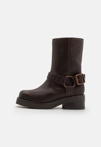 Bruine leren enkellaars met een ronde neus, decoratieve gespsluiting en een chunky hak. Gladde textuur met zichtbare stiksels.