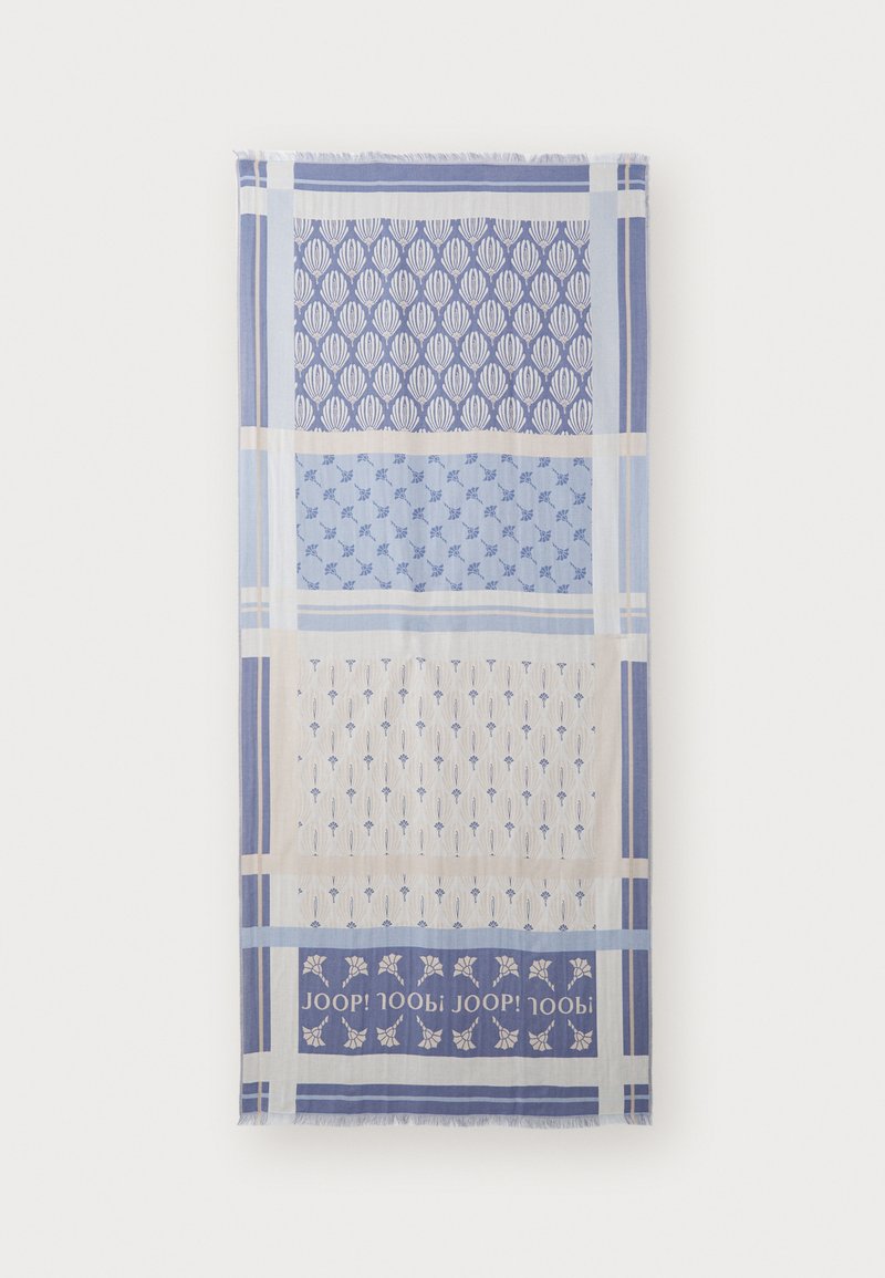 Textile scarf featuring alternating patterns in blue and cream, with leaf and floral motifs. Edges are fringed. Logo displayed at the bottom.