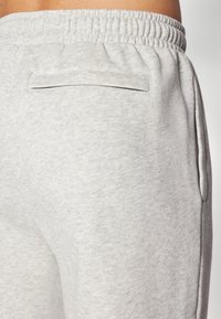 Lysegrå sweatpants lavet af blødt stof, med elastisk talje, sidelommer og en enkelt baglomme med åbning.
