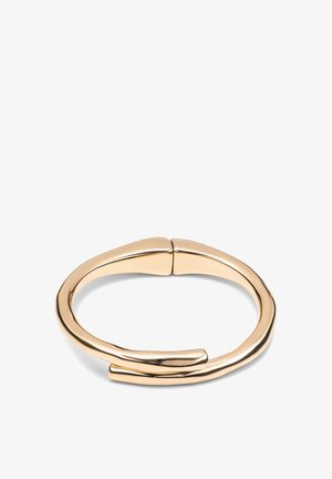 Bracelet en métal doré avec un design lisse et courbé. Présente un espace au niveau de la fermeture, mettant en avant sa forme minimaliste et sa finition polie.