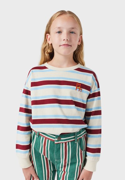 Langsleeve gestreepte shirt met crèmekleurige, blauwe en bordeauxrode strepen, met een kleine geborduurde stoel. Gecombineerd met groen en rode gestreepte broek.