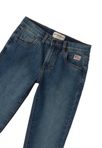 Jeans in denim di un blu medio con cuciture a contrasto, dotati di un'etichetta sulla cintura e di un piccolo patch sulla tasca anteriore.