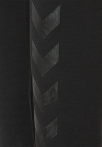 Zwarte broek met een textuurstof en matte zwarte chevronaccenten langs de zijkant, die een contrasterend designelement creëren.