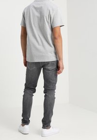 Šedé polo tričko s krátkým rukávem v kombinaci s tmavě šedými slim-fit džíny a bílými teniskami. Oblečení má neformální a pohodlný vzhled.