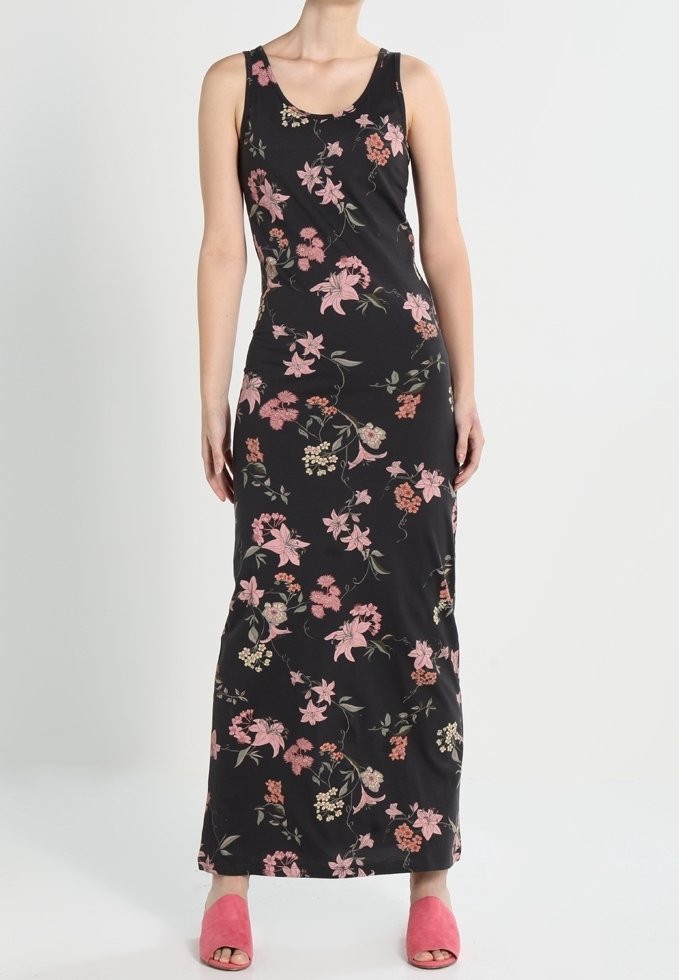 Robe maxi noire sans manches avec imprimé floral rose et beige portée avec des sandales ouvertes rose sur fond uni.