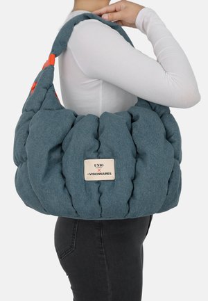 Gesteppte blaue Textiltasche mit weicher, voluminöser Form, versehen mit einem orangefarbenen Akzent am Riemen und einem Etikett mit Markendetail.