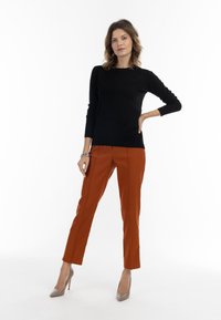 Zwarte lange mouwen sweater gecombineerd met oranje op maat gemaakte broek en crèmekleurige hoge hakken. Gladde stof en gestructureerd ontwerp met details in de zijnaad.
