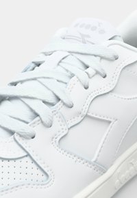 White leather athletic shoe with textured accents, zigzag design, flat white laces, and small perforations on the toe area.