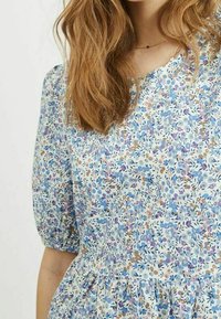 Robe à manches courtes à motif floral en bleu clair, avec des accents violets, roses et verts, taille froncée et texture de tissu douce.