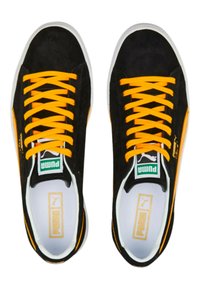 Mustat mokkakengät, joissa on kirkkaan oranssit nauhat, valkoinen kumipohja ja hienovarainen brändäys sivuilla ja kielellä. Klassinen matala malli.