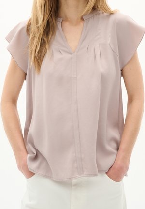 Blusa di un leggero color malva con maniche corte e svolazzanti, colletto a V e dettagli a pieghe. Tessuto morbido con una vestibilità rilassata, indossata sopra pantaloni bianchi.