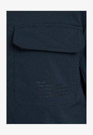 Marineblauwe shirt met een grote zak en reliëftekst op de zak die merk en kenmerken beschrijft; gladde, duurzame stof.