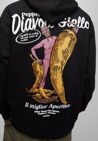 Nadruk na plecach bluzy z kapturem przedstawiający różowego diabła trzymającego duże żółte papryczki chili oraz włoski tekst promujący "Il miglior Aperitivo" w Padwie, Włochy.