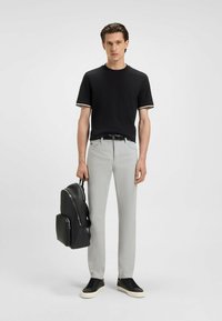 Czarny t-shirt z krótkim rękawem z białym i beżowym wykończeniem, jasnoszare spodnie, czarny plecak z zamkiem błyskawicznym oraz czarne trampki z kremową podeszwą.