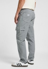 Pantalones cargo grises con múltiples bolsillos, un corte relajado y costuras visibles. Combinados con zapatillas blancas con acentos negros.