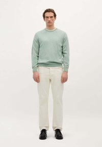 Helles grünes Rundhals-Sweatshirt aus weichem Stoff, kombiniert mit cremefarbene Hosen und schwarzen Schuhen. Das Outfit hat eine lockere Passform.