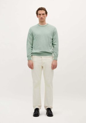 Pull ras du cou vert clair en tissu doux, associé à un pantalon crème et des chaussures noires. La tenue présente une coupe décontractée.