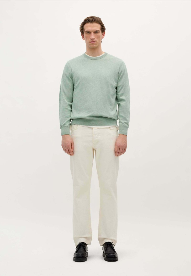 Helles grünes Rundhals-Sweatshirt aus weichem Stoff, kombiniert mit cremefarbene Hosen und schwarzen Schuhen. Das Outfit hat eine lockere Passform.