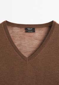 Brązowy sweter z kaszmiru z dekoltem w serek. Charakteryzuje się delikatną fakturą i prążkowanymi akcentami wokół szyi. Metka widoczna wewnątrz kołnierza.