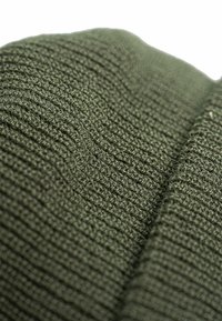 Neulottu kangas syvässä oliivinvihreässä, jossa on tekstuurinen, ribbikuvio. Sujuva kudonta näkyvillä saumatiedoilla, luoden syvyyttä ja ulottuvuutta.