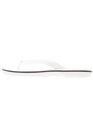 Sandale tongs blanche avec une bande noire le long de la semelle, vue de côté sur fond blanc.