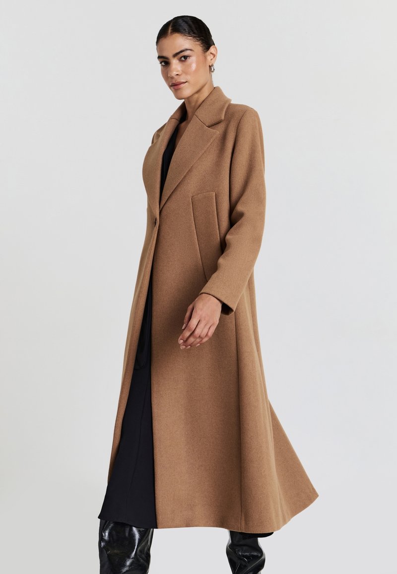 Cappotto lungo in un morbido tessuto misto lana. Presenta un colletto a revers, chiusura con un solo bottone e due tasche laterali per la funzionalità.