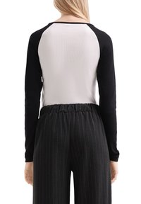 Frau, die ein langärmeliges, schwarz-weißes Raglan-Shirt und schwarze elastische Hosen mit Nadelstreifen trägt, von hinten gezeigt.