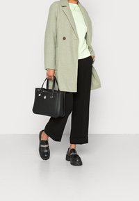 Abrigo verde claro texturizado sobre una sudadera a juego, pantalones negros de pierna ancha, bolso negro y mocasines negros con detalle de cadena.